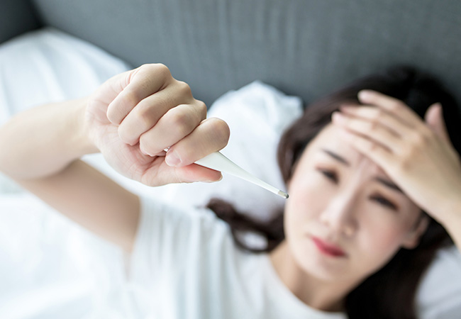 額に手をあて体温計を見上げる女性